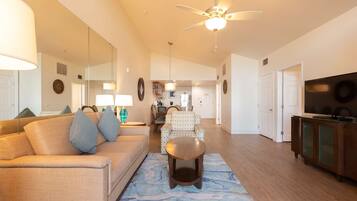 A spacious living room with a sofa, a coffee table, a ceiling fan, and a kitchen in the background.