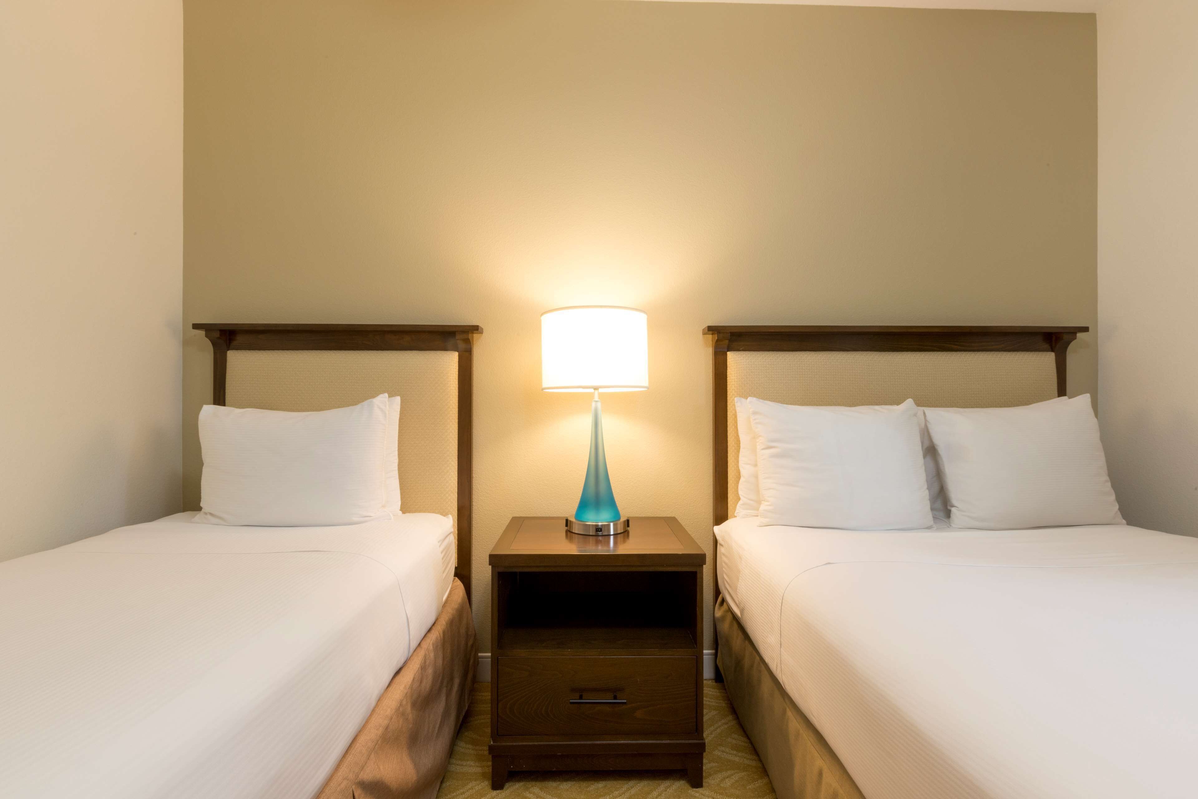 A hotel room with two single beds, a nightstand with a lamp, and a small drawer.