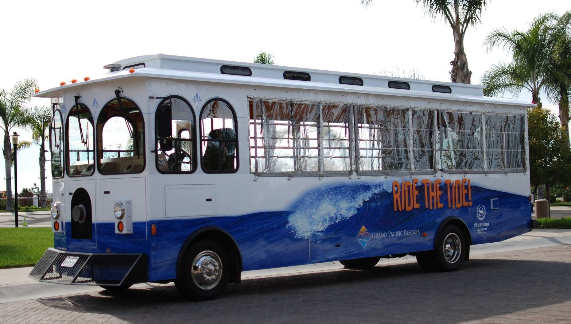 Een bus met een blauw-wit kleurenschema, reclame maakt voor 'Ride the Tide' en 'Grand Pacific Resorts'.