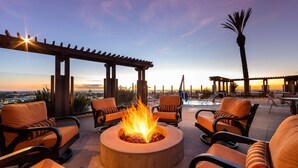 A rooftop terrace with a fire pit, outdoor seating, and a view of the sunset. - Grand Pacific Palisades (Carlsbad)