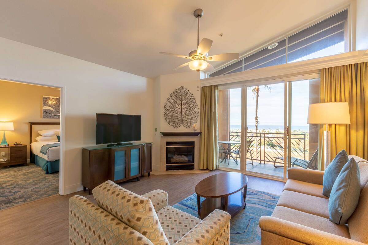 A hotel room with a sofa, a coffee table, a TV, a fireplace, and a balcony with a view.