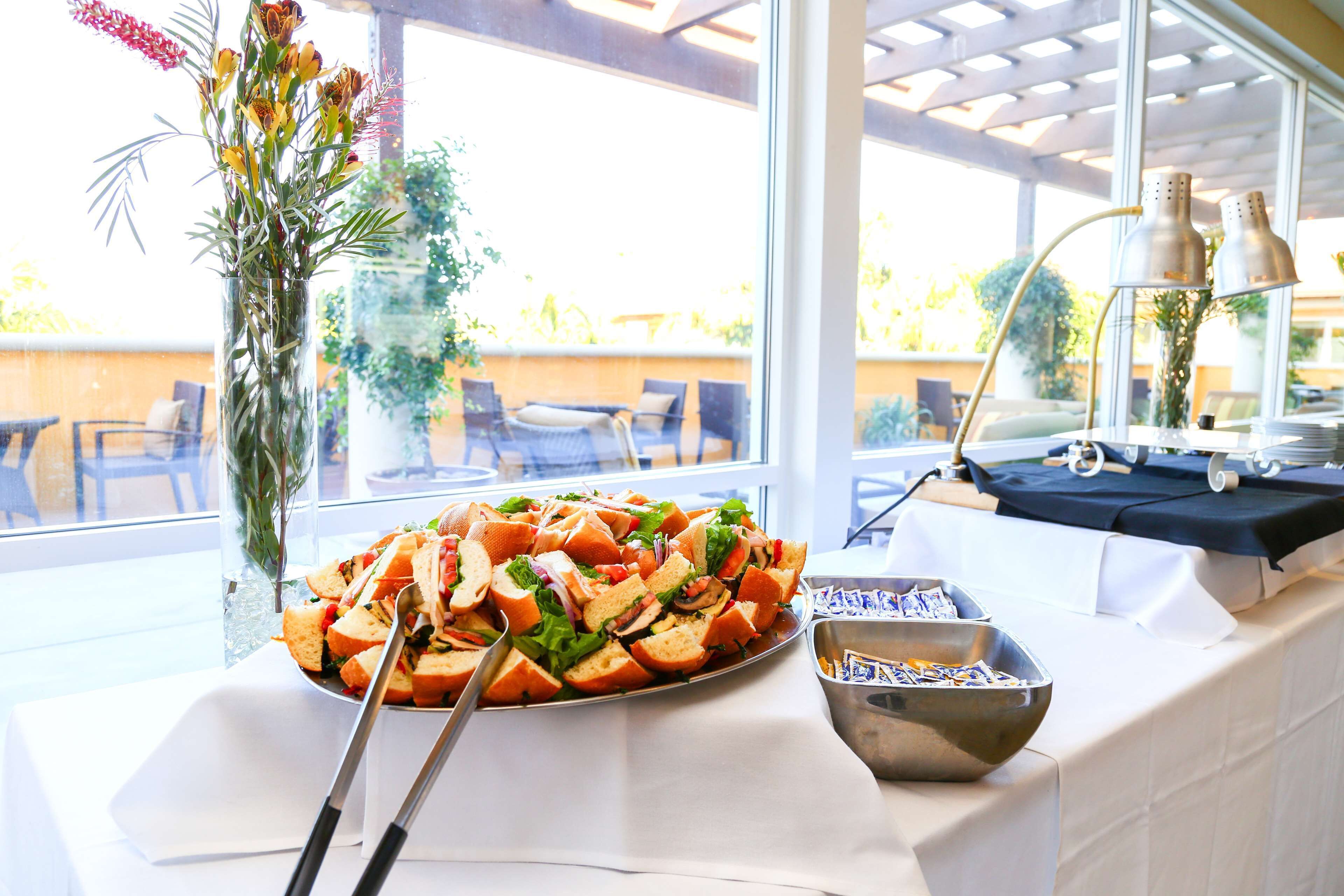 A buffet table with a salad, a vase with flowers, and a bowl of condiments.