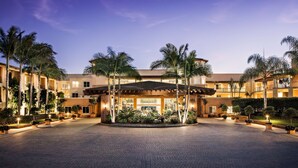 A hotel with a central courtyard, palm trees, and a well-lit entrance. - Grand Pacific Palisades (Carlsbad)