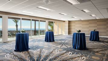 A spacious room with large windows, a patterned carpet, and three tables with blue tablecloths.