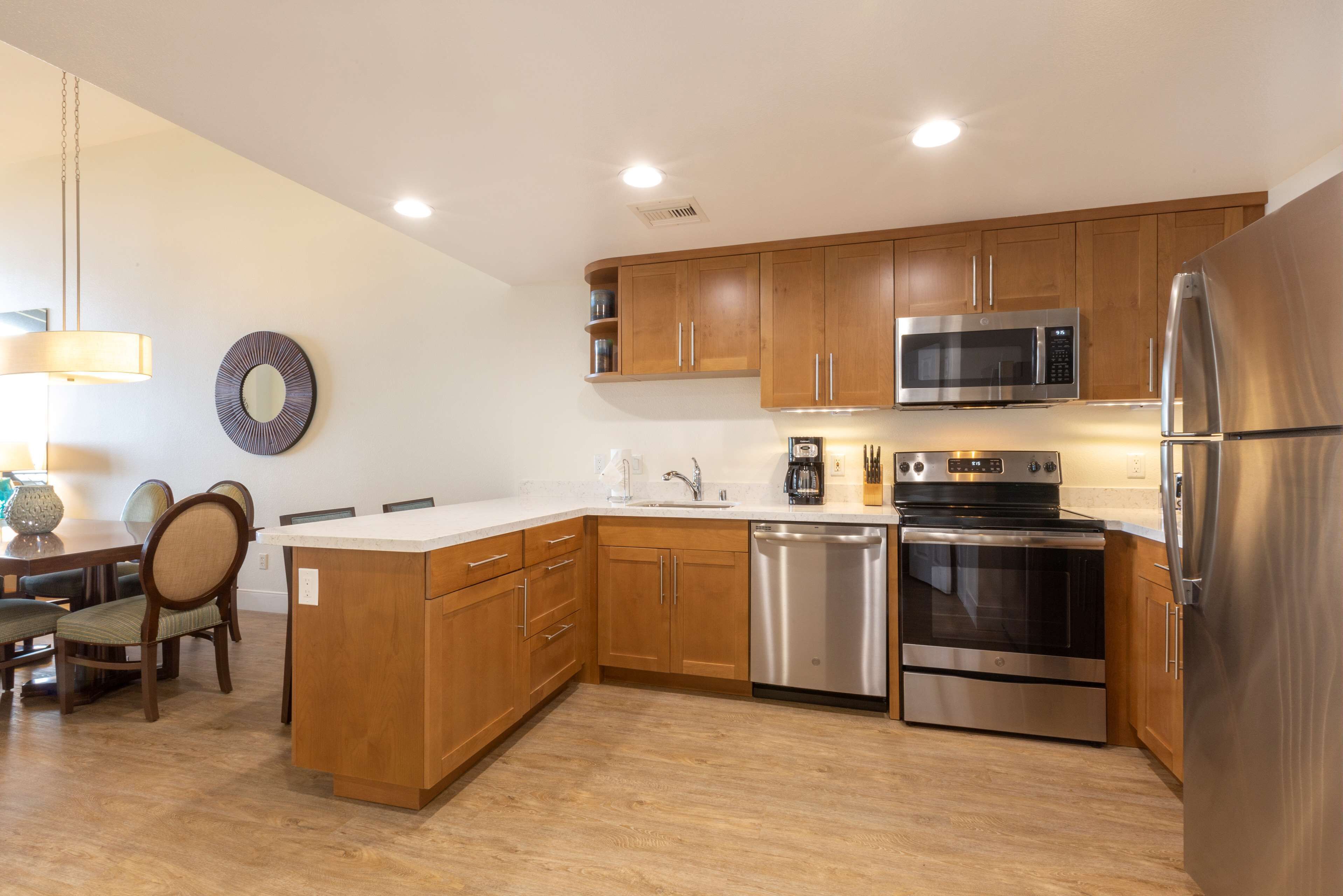 A modern kitchen with wooden cabinets, stainless steel appliances, and a dining area with chairs and a table.