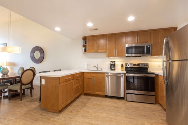 A modern kitchen with wooden cabinets, stainless steel appliances, and a dining area with chairs and a table.
