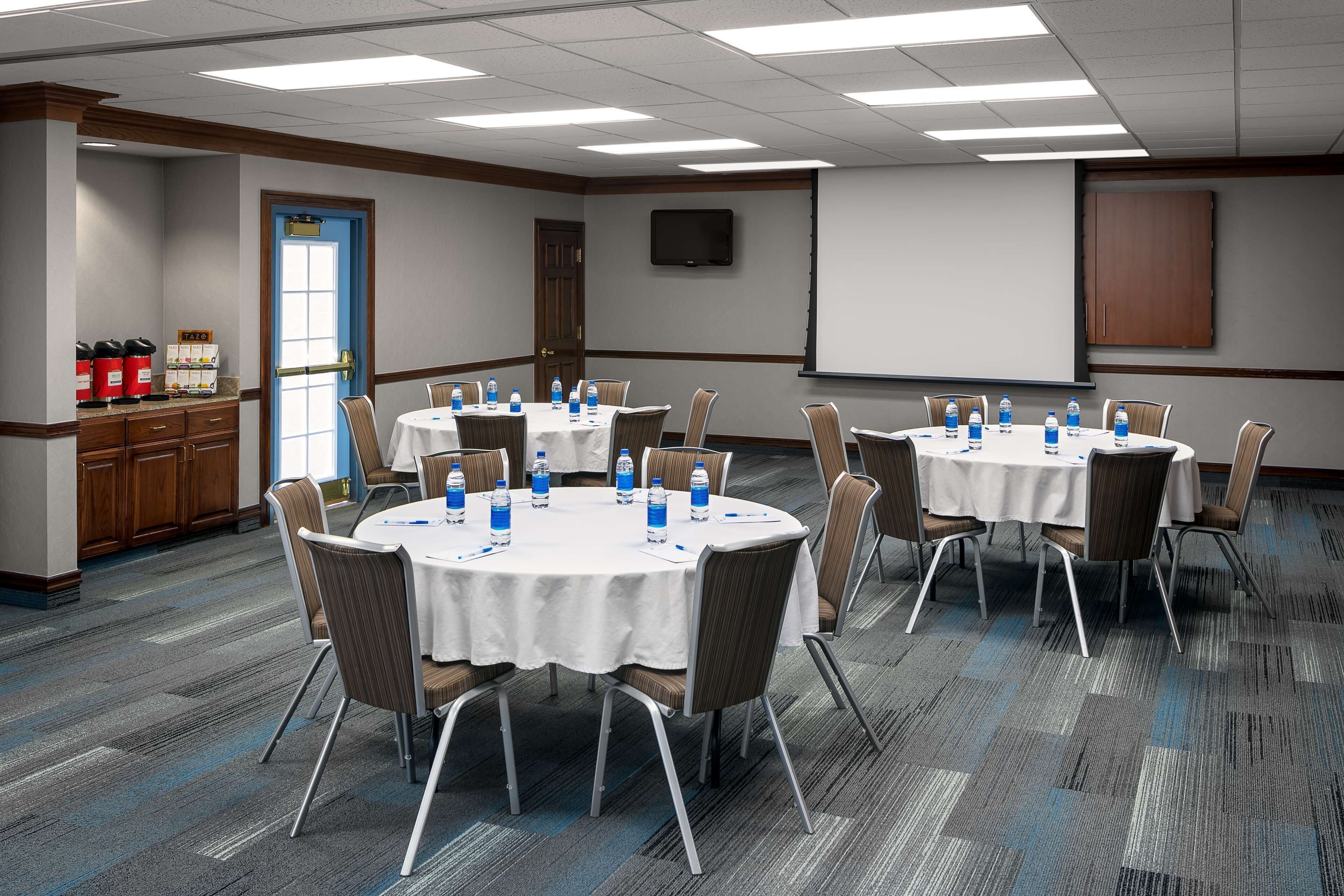 A conference room with round tables, chairs, and a projector screen.