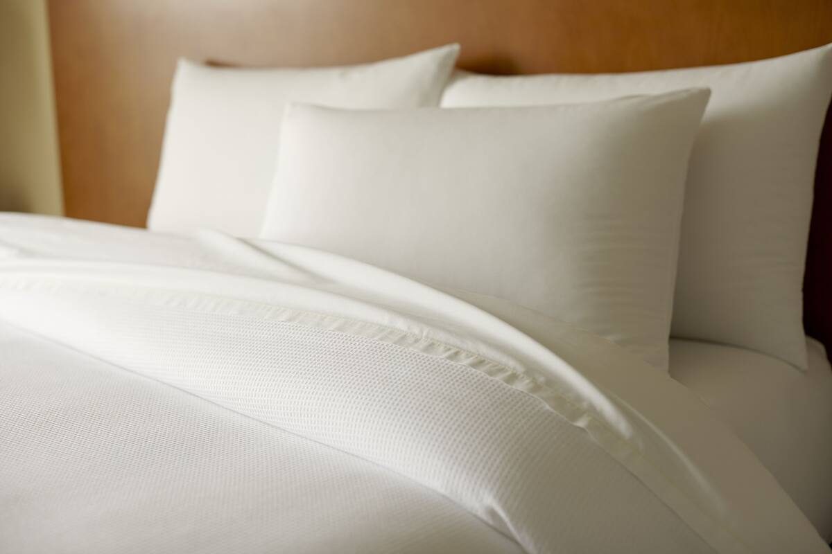 A neatly made bed with white linens and pillows.