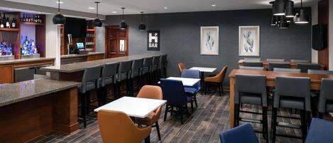 A modern bar area with a counter, seating, and a herringbone-patterned wall.