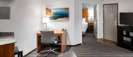 A hotel room with a desk, chair, and a painting of a landscape.