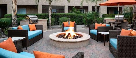 An outdoor seating area with wicker furniture, a central fire pit, and a barbecue grill.