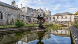 A historic stone building with a moat and a statue in the foreground. - Hazlewood Castle & Spa (Tadcaster)