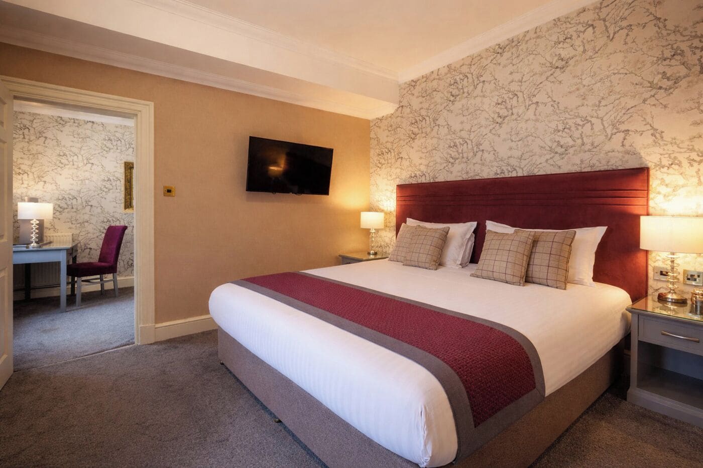 Ein Hotelzimmer mit einem großen Bett, einem an der Wand montierten Fernseher und einem Schreibtisch mit Stuhl.