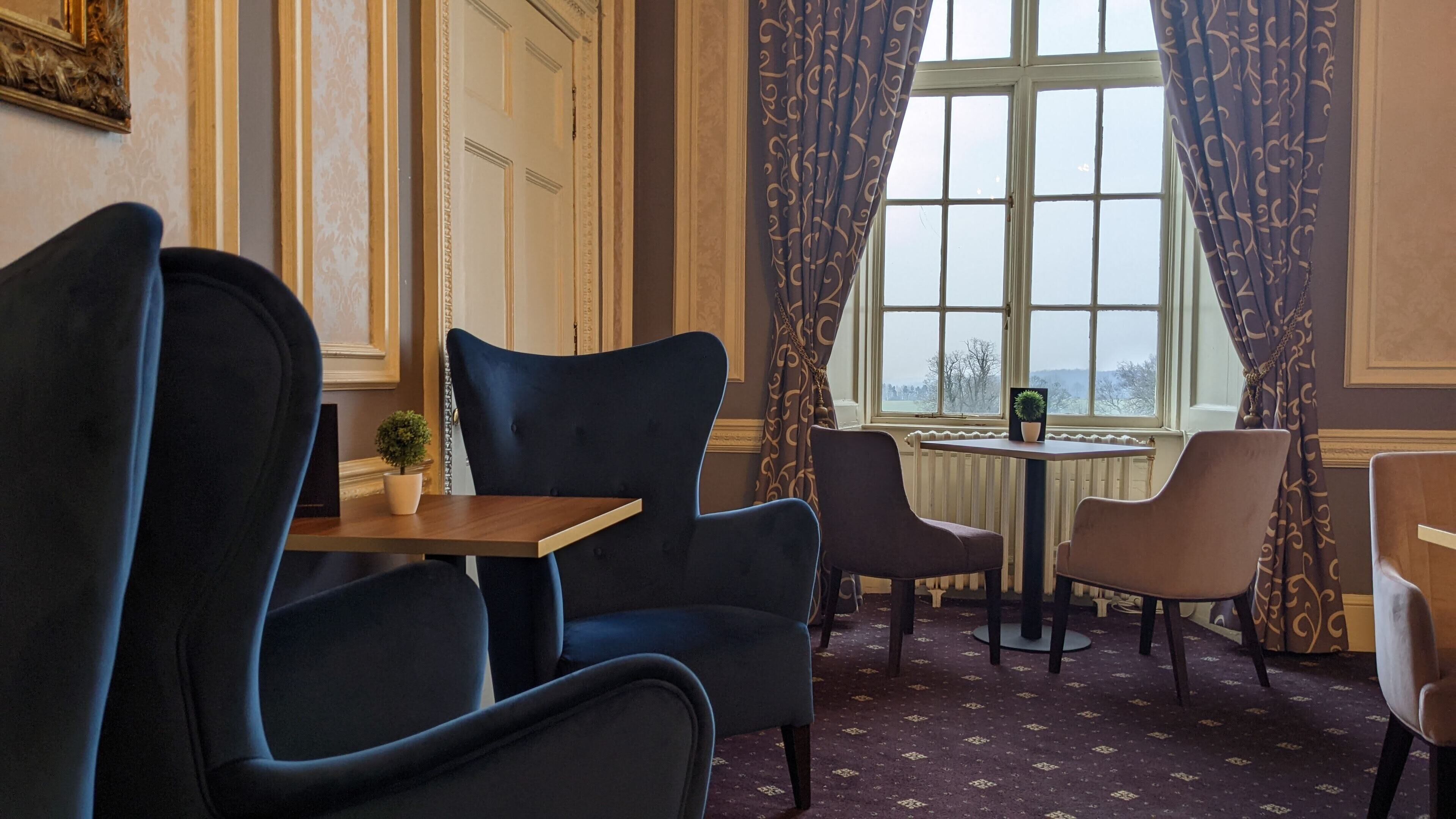 Una habitación con una mesa y sillas, una ventana con cortinas y vistas a árboles.