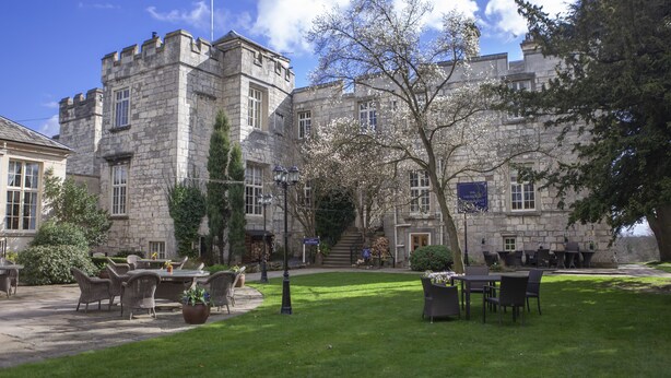 A stone building with a courtyard, outdoor seating, and a flag. - Hazlewood Castle & Spa (Tadcaster)