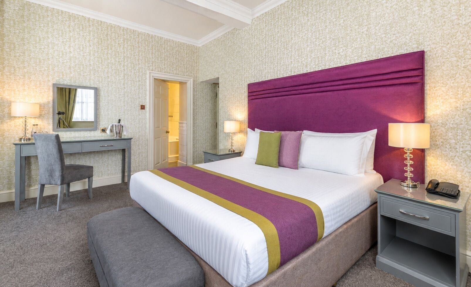 A hotel room with a bed, bedside tables, a desk, a chair, and a mirror.