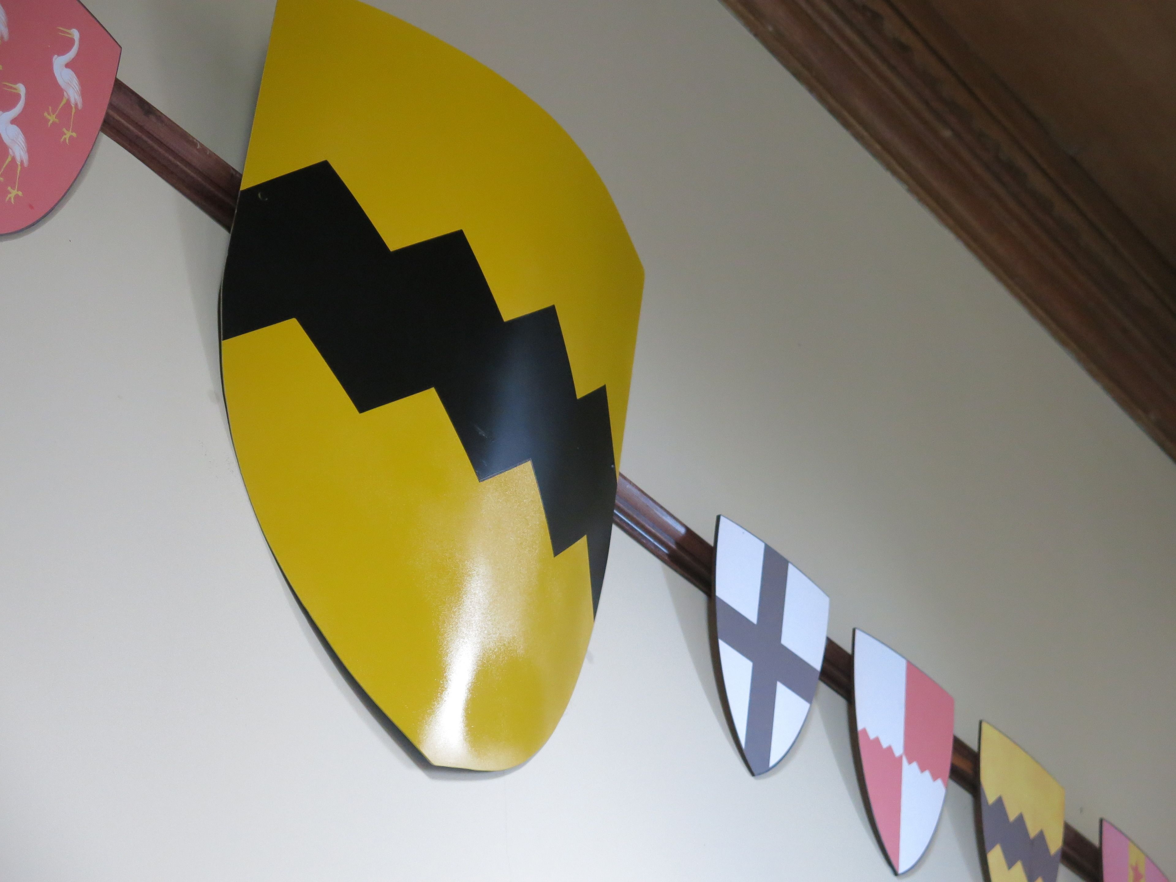 A wall with a series of decorative shields and a large yellow shield with a black zigzag pattern.