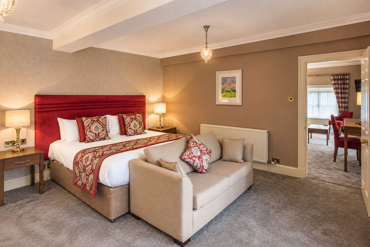 A hotel room with a large bed, a sofa, a nightstand, a lamp, a picture on the wall, and a view of the dining area.
