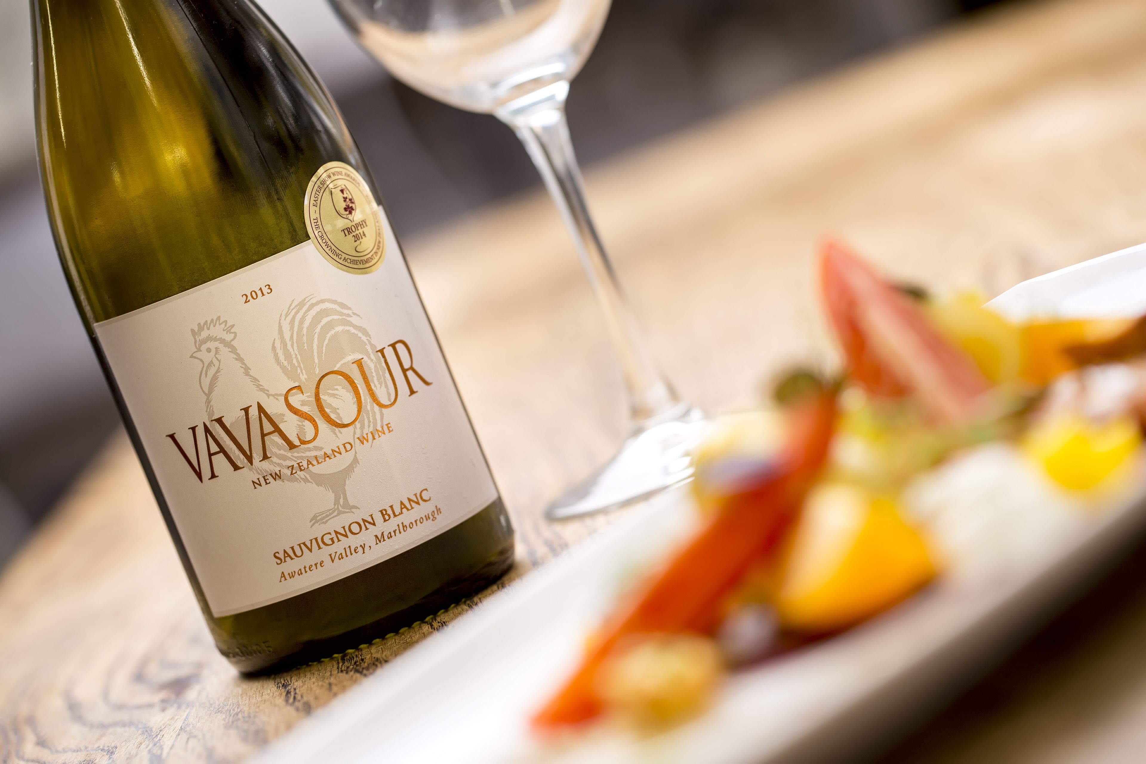 Una botella de vino blanco Sauvignon Blanc Vavasour y una copa de vino sobre una mesa con un plato de comida.