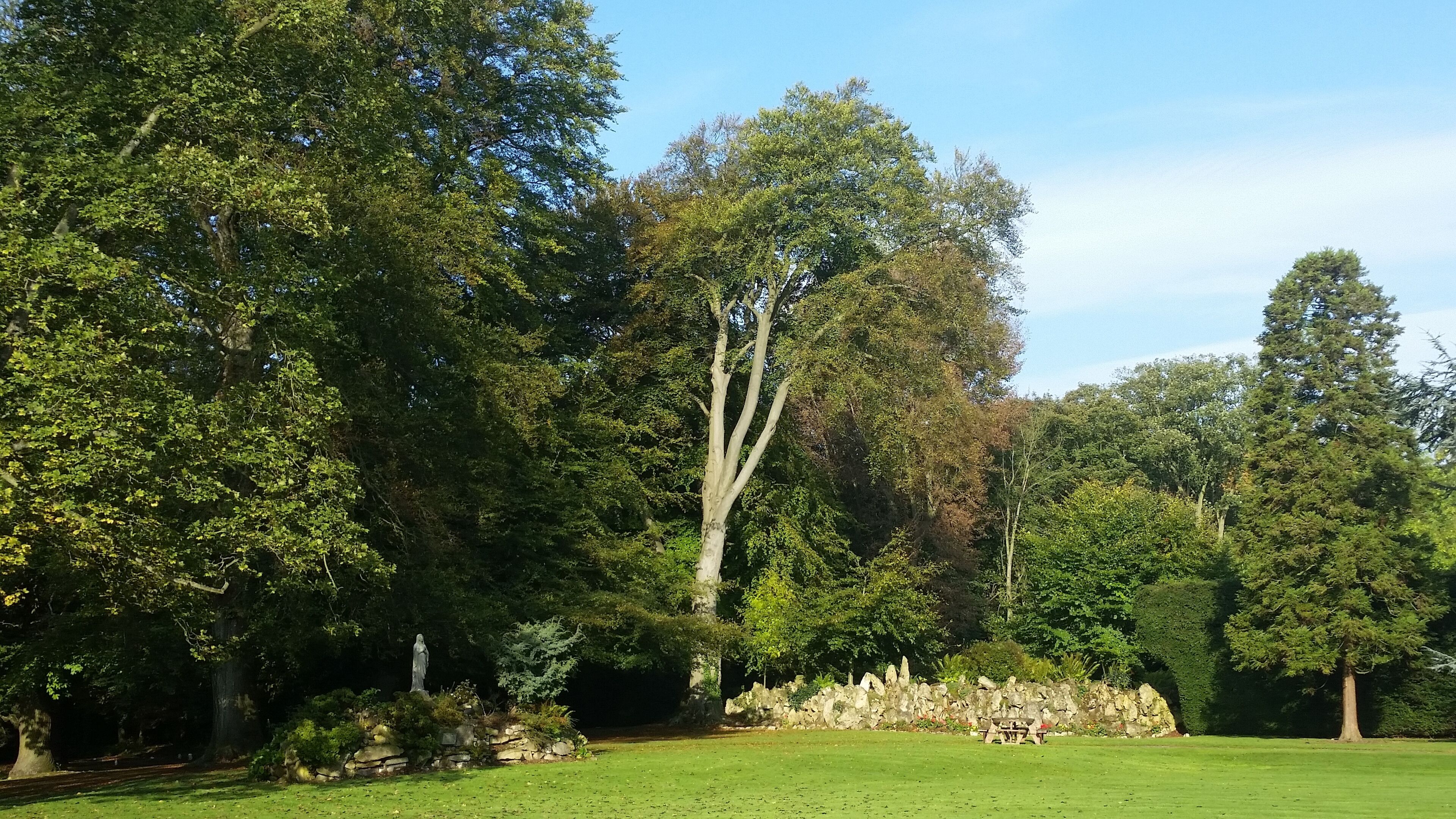 A park with a statue, a picnic area, and a stone wall.