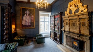 A library with a fireplace, bookshelves, a chandelier, and a large portrait. - Hazlewood Castle & Spa (Tadcaster)