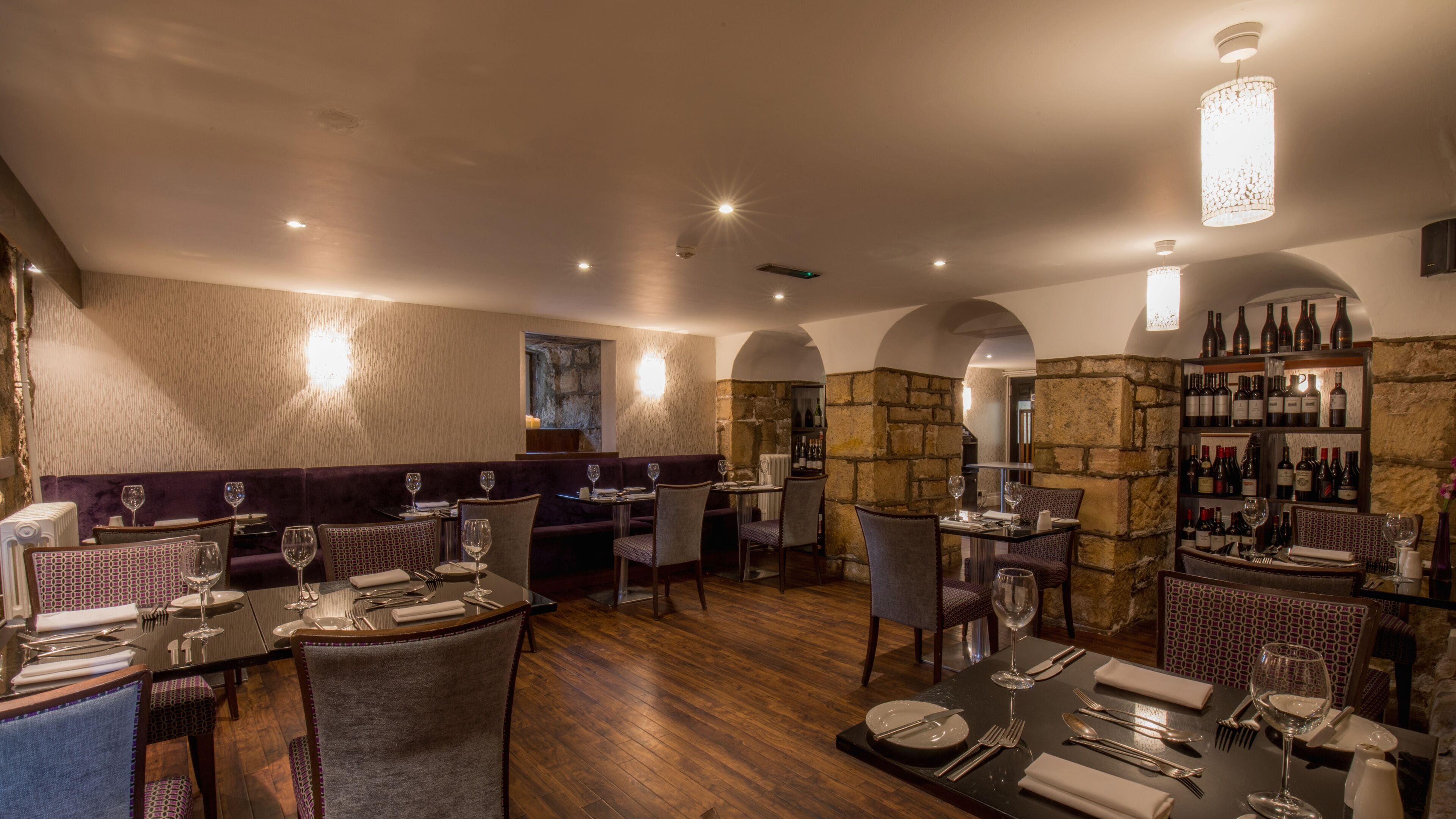 Ein Restaurant mit Holzboden, gedeckten Tischen und einer Weinauslage.