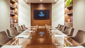 Un salón de conferencias con una mesa larga, sillas y una pantalla de televisión que muestra '4 MANTO HOTEL-LUMA'.