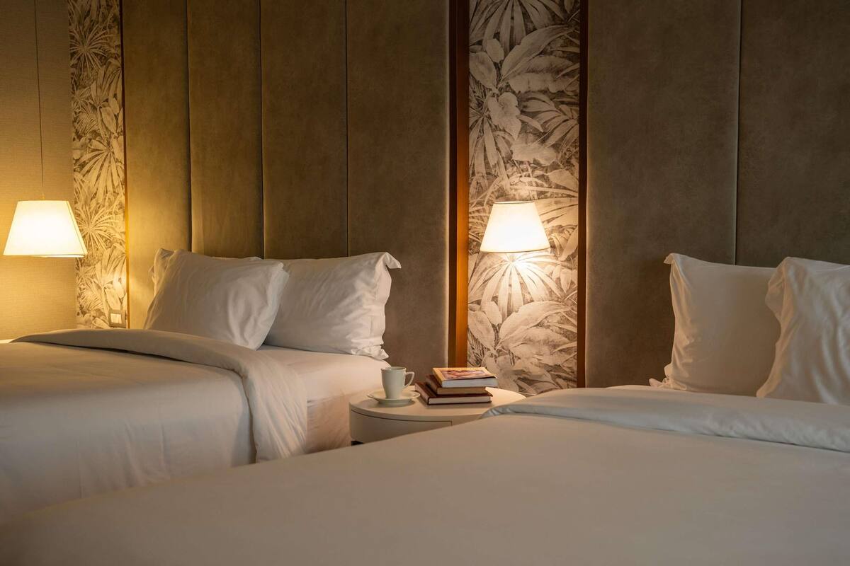 A hotel room with two beds, a nightstand with a lamp, and a wall with a floral pattern.