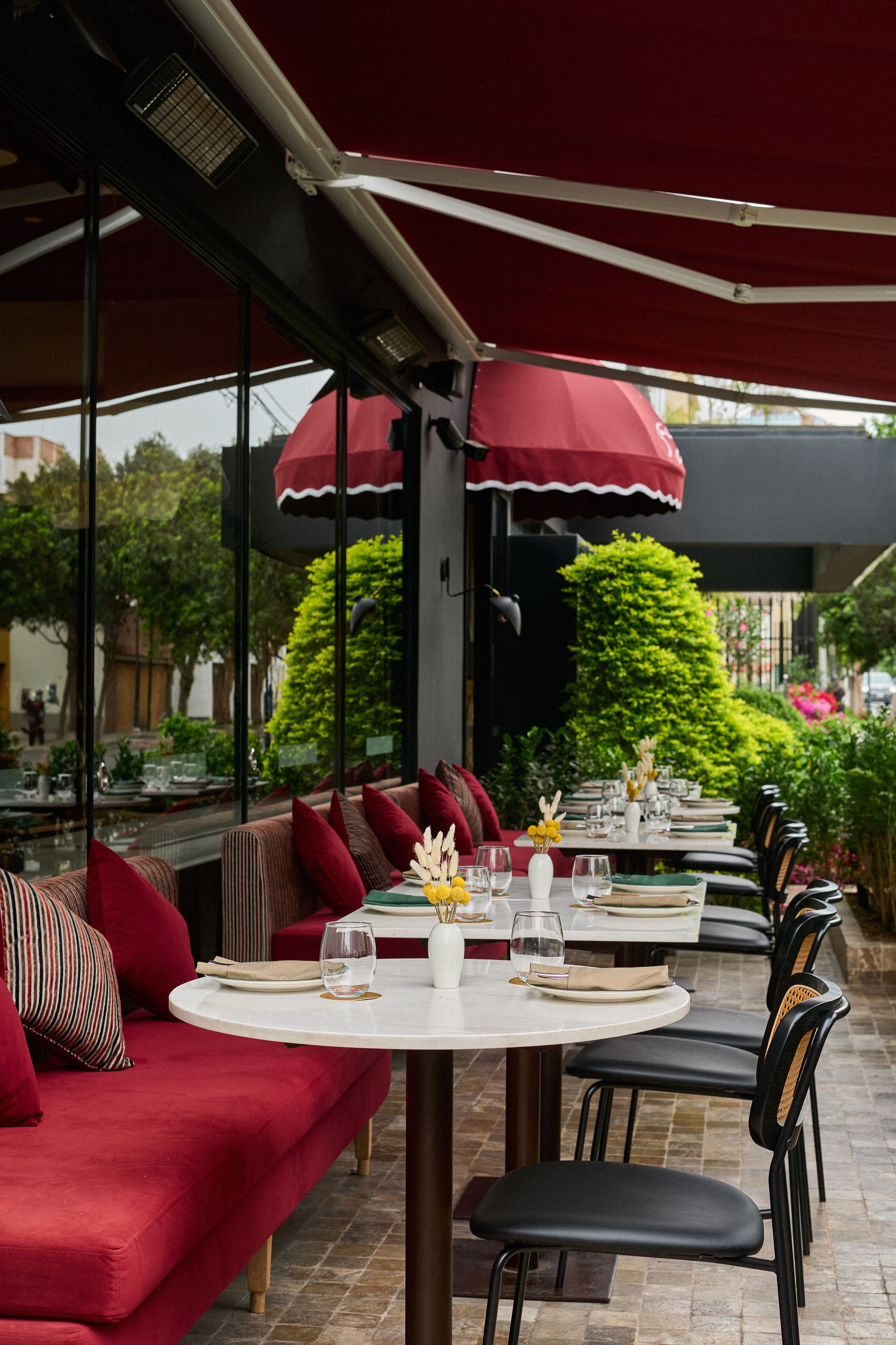 An outdoor dining area with red upholstered seating, white tables, and black chairs.