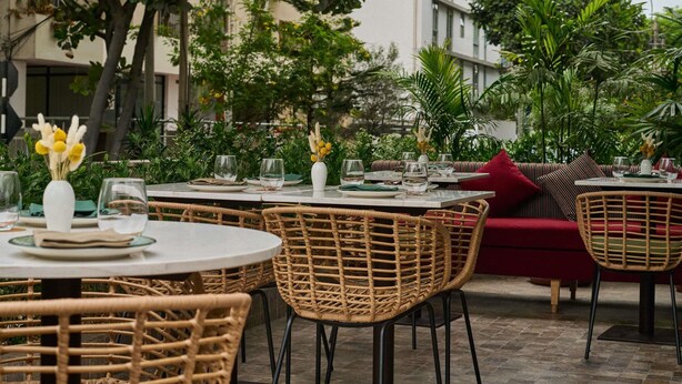 Outdoor dining tables with wicker chairs, a red sofa, and a white vase with flowers. - Manto Hotel Lima - MGallery  Collection (Lima)