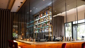 A bar area with a wooden counter, red bar stools, and a glass display case filled with bottles. - Manto Hotel Lima - MGallery  Collection (Lima)