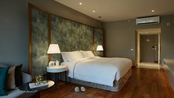 Een hotelkamer met een groot bed, twee bedlampen, een kleine tafel met een lamp, een bank en een paar slippers op de vloer.