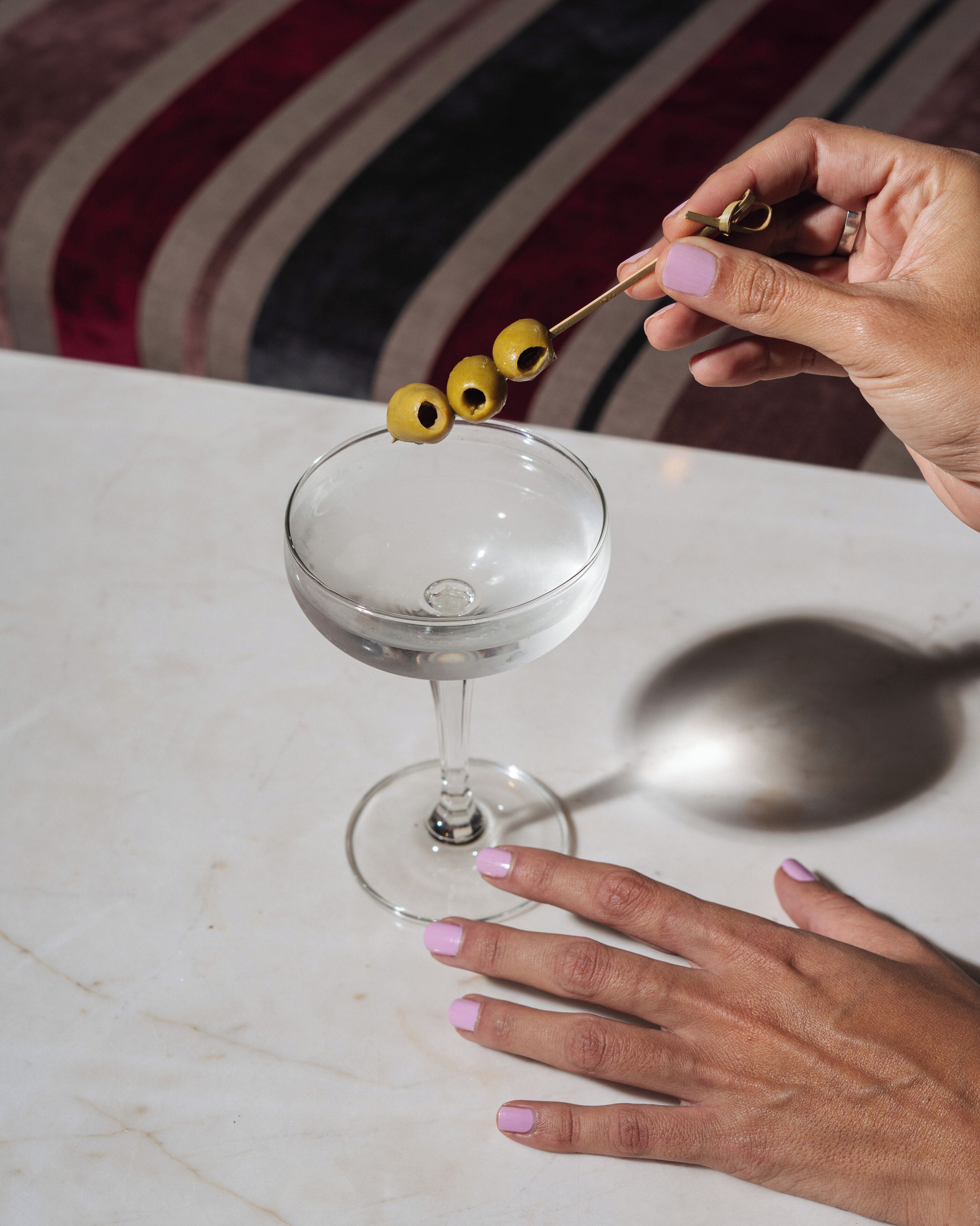 A hand holding a cocktail shaker with olives.