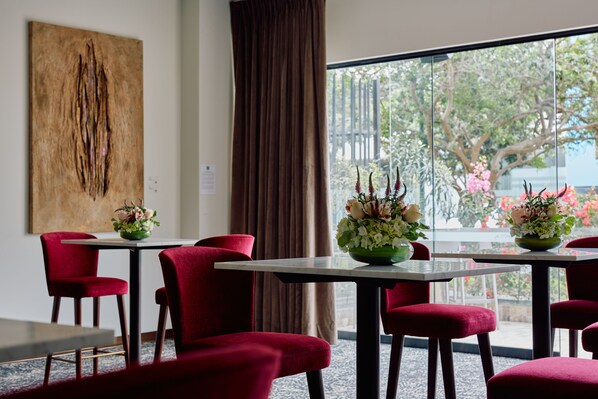 Un espace repas avec des chaises à revêtement rouge, des tables blanches et des centres de table ornés de motifs floraux.