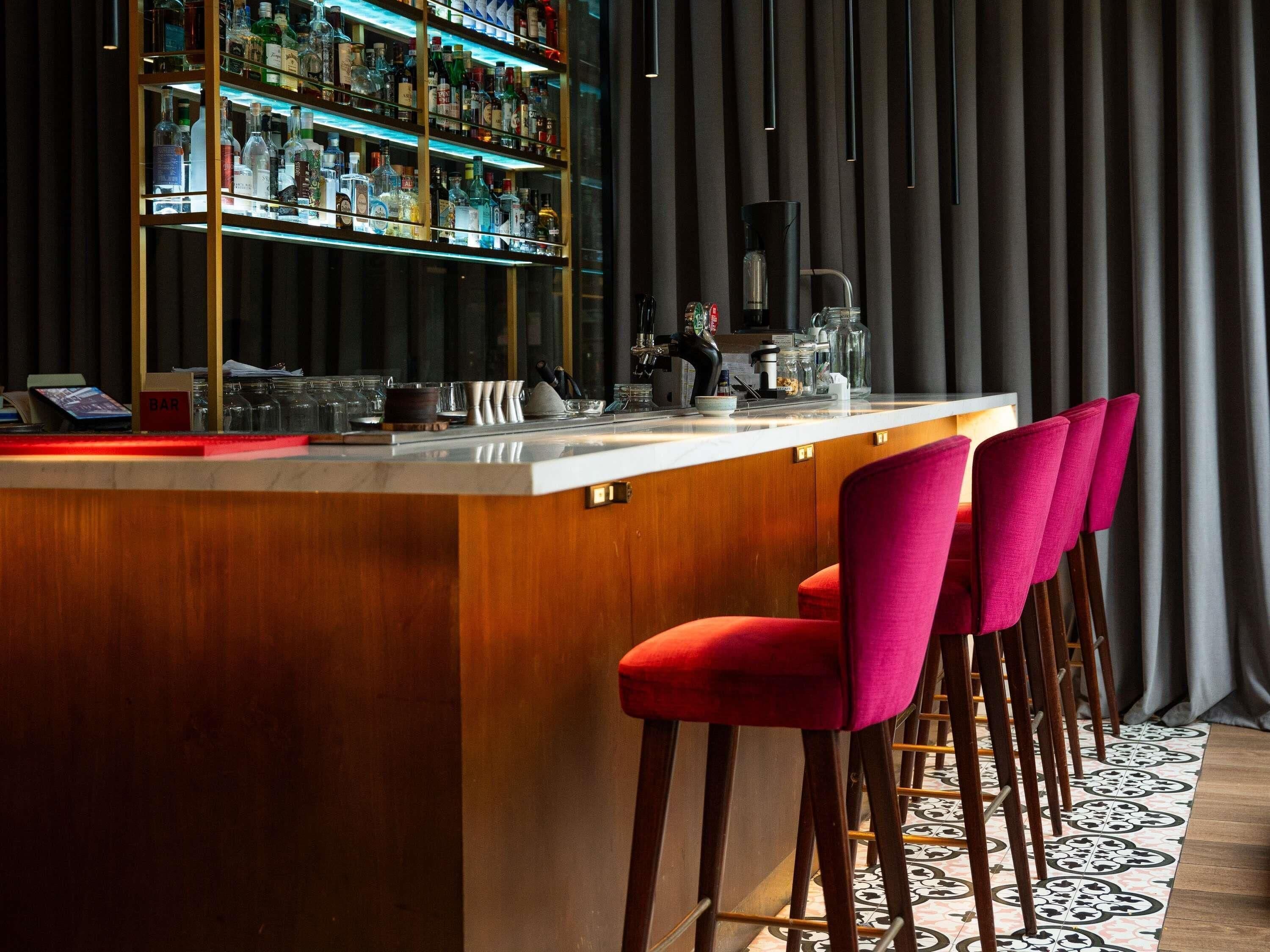 A bar area with a wooden counter, bar stools, and a shelf of liquor bottles.