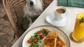 A wicker chair, a white table, a plate with food, a cup of coffee, and a glass of juice.
