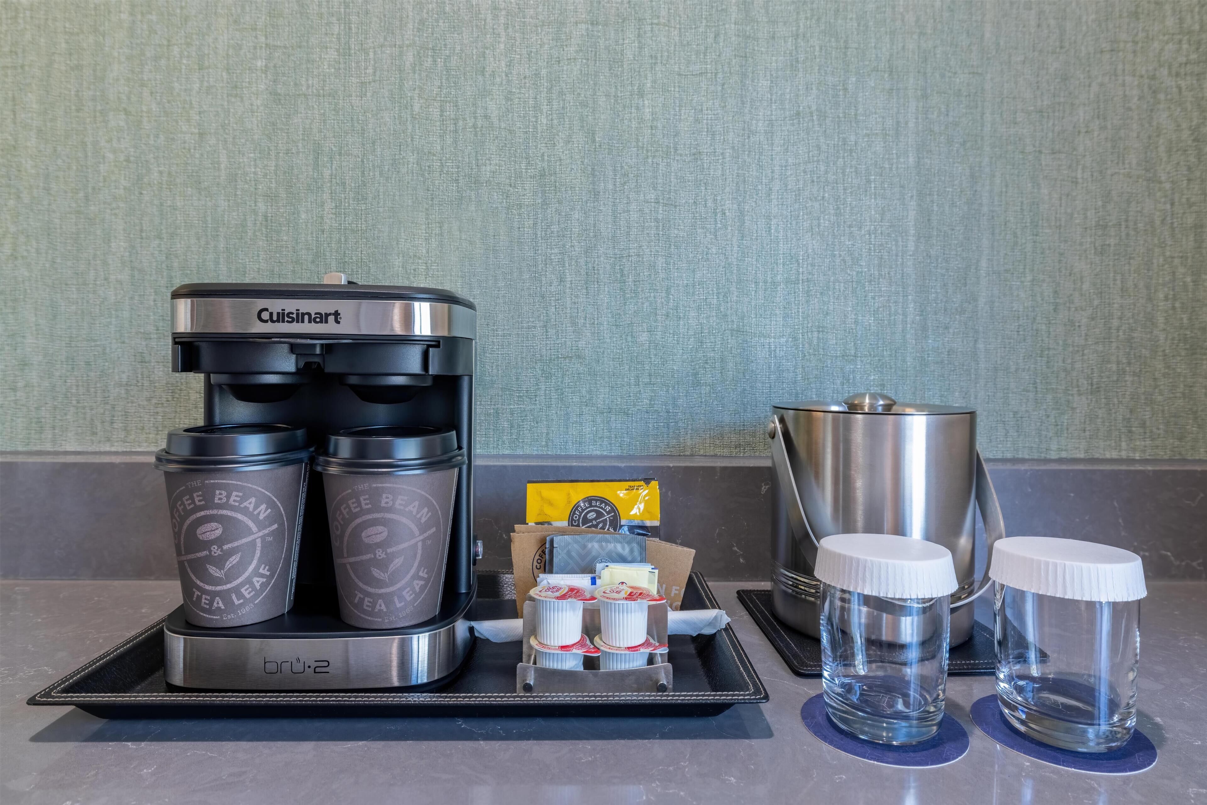 A coffee maker, two coffee cups, a kettle, and two glasses on a tray.
