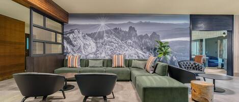 A modern living room with a green sofa set, two black armchairs, a wooden coffee table, and a large mountain landscape mural on the wall.