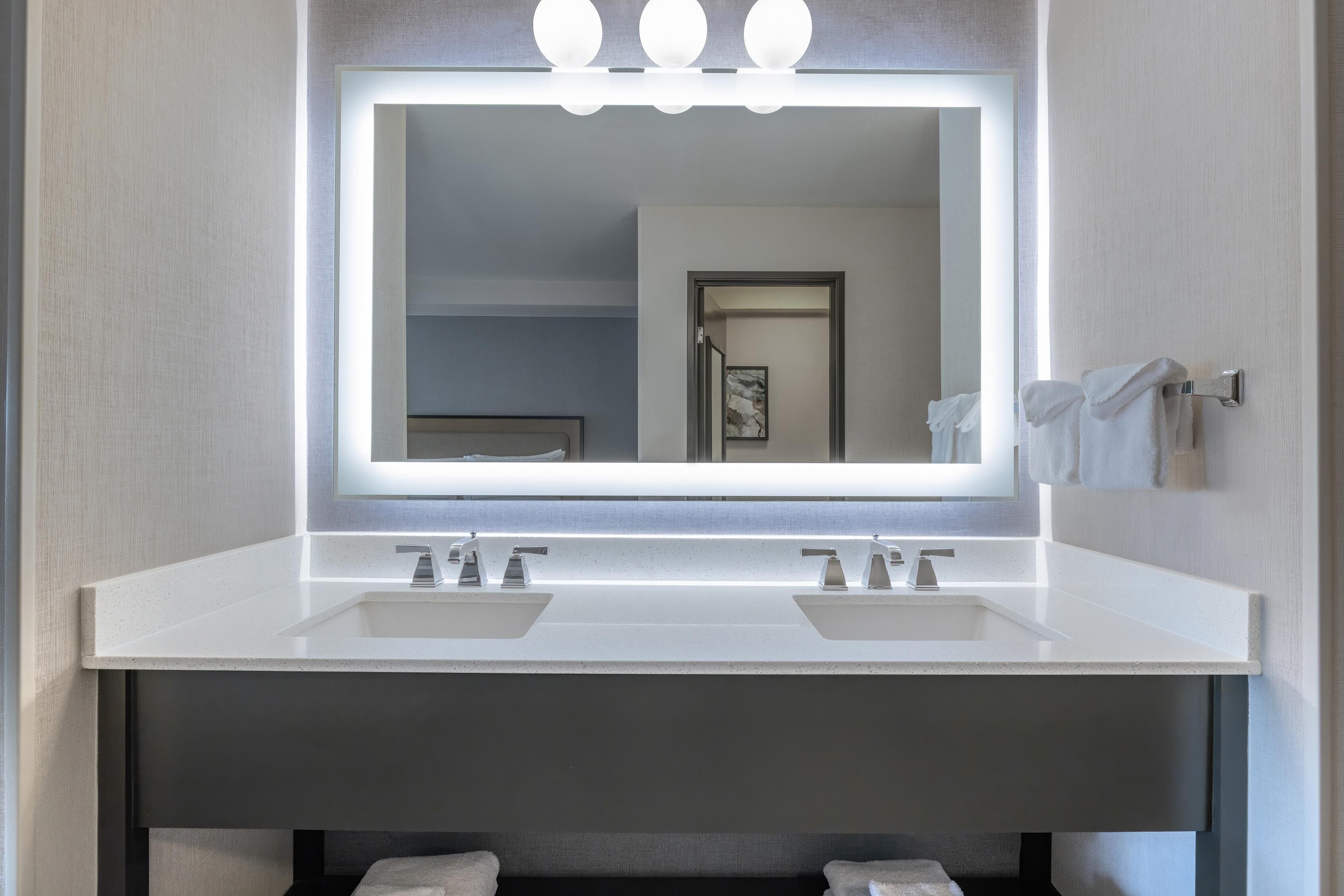 A modern bathroom with a large mirror, two sinks, and overhead lighting.