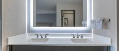 A modern bathroom with a large mirror, two sinks, and overhead lighting.