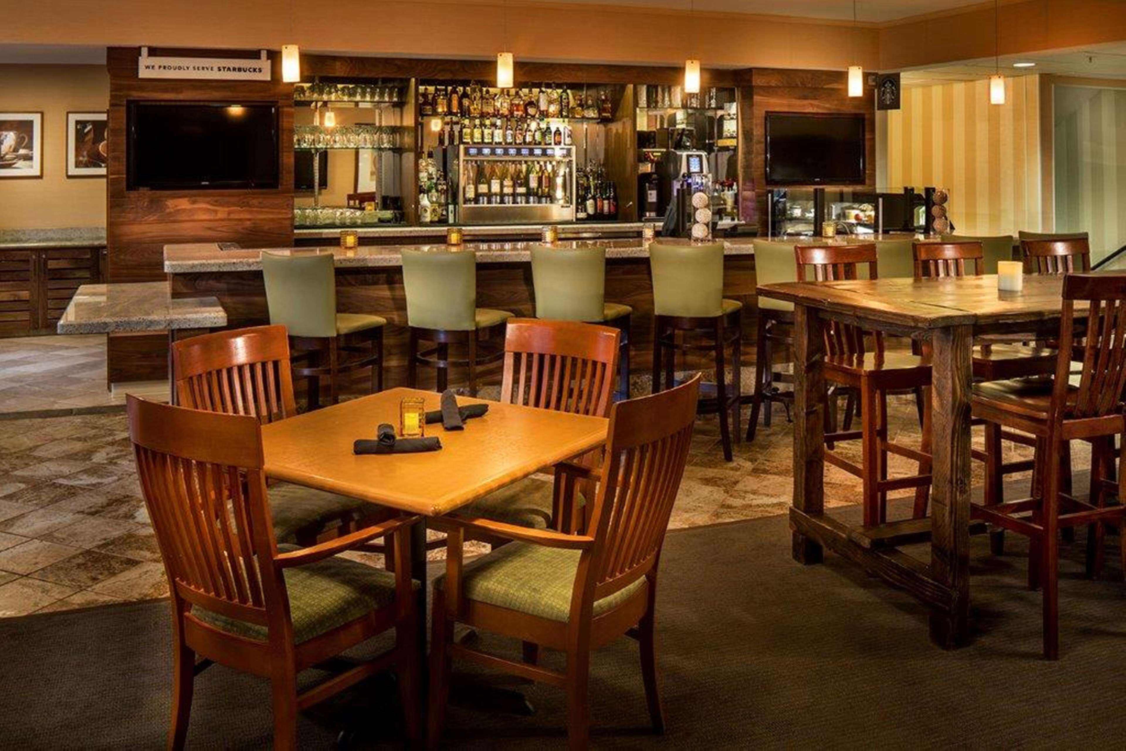 A bar area with multiple seating options, including bar stools and tables, and a television mounted on the wall.