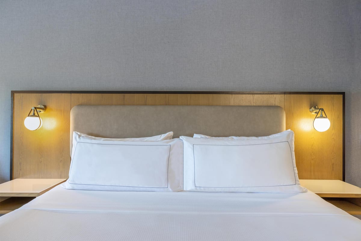 Cama bem arrumada com duas almofadas, cabeceira de madeira e duas luminárias de cabeceira.
