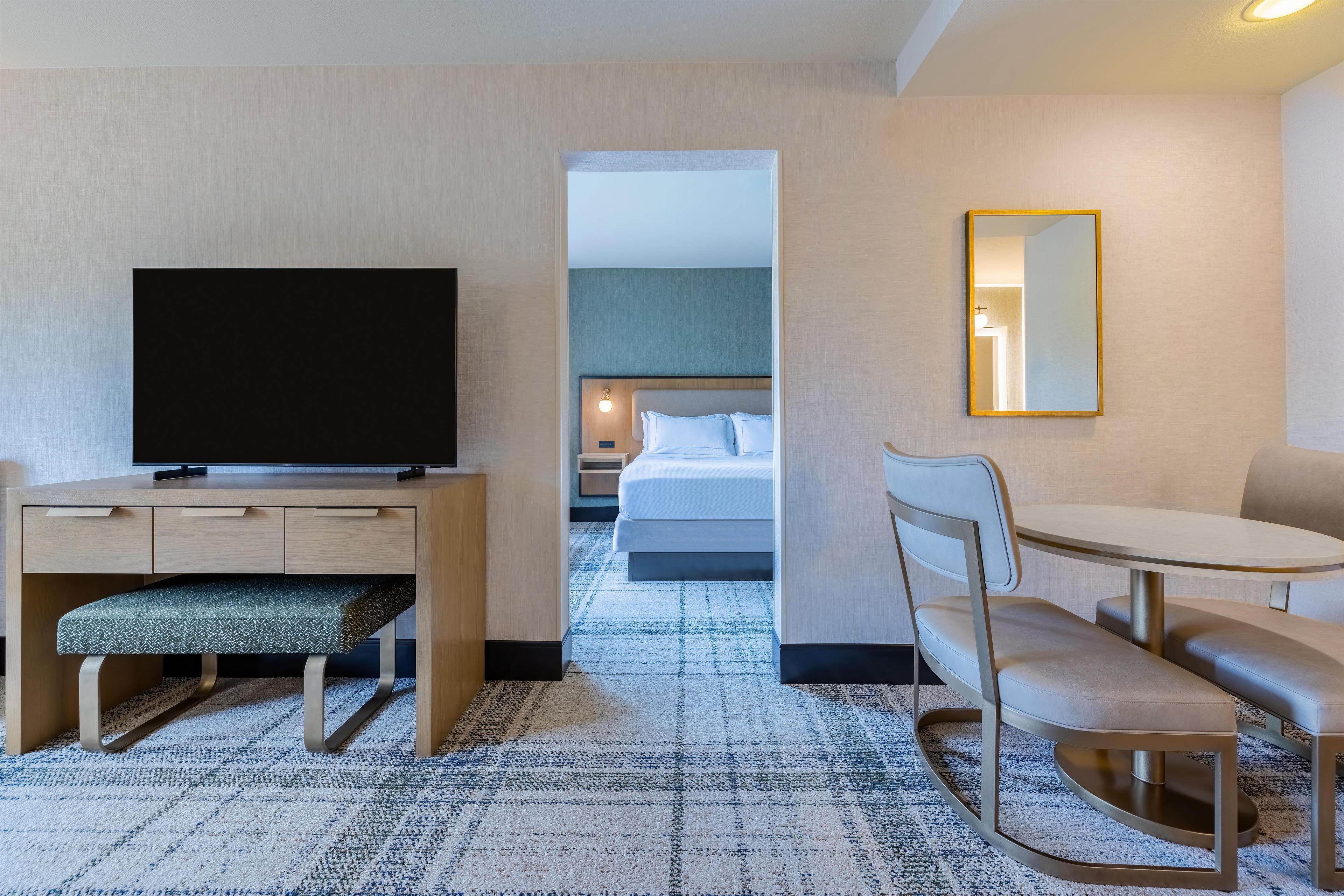 A hotel room with a desk, television, seating area, and a bed.