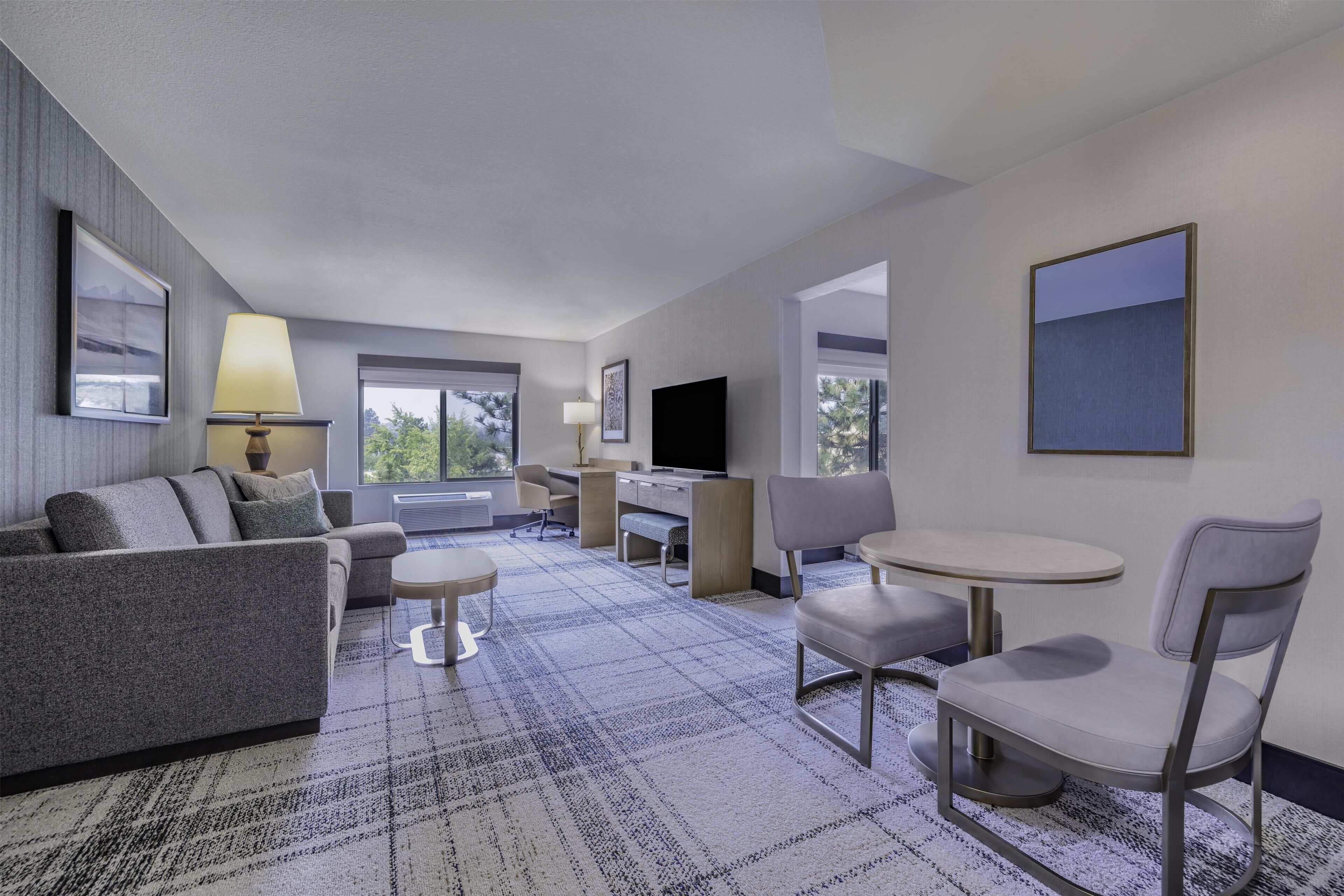 A hotel room with a sofa, a desk, a TV, a chair, and a small table.