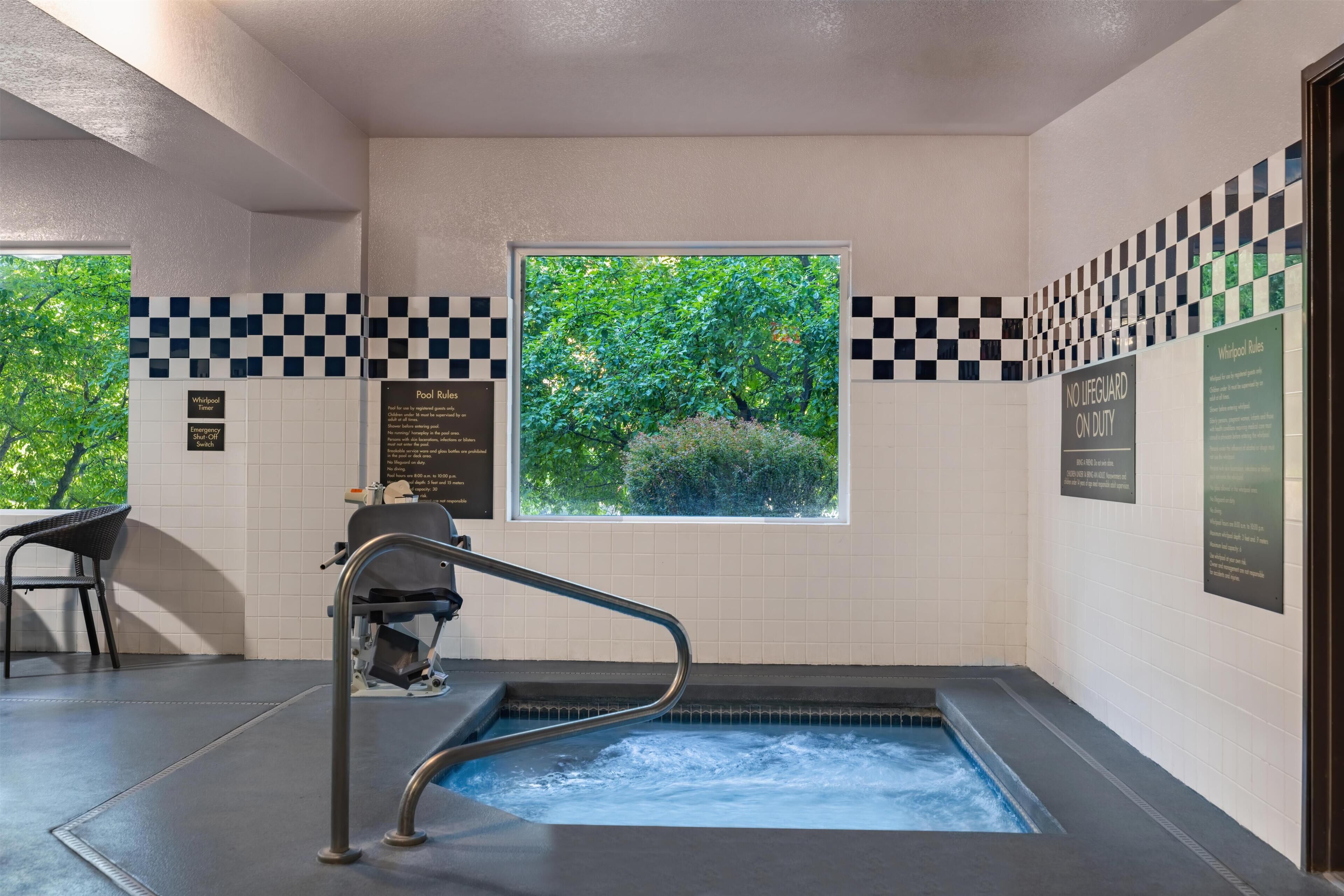 Un área de spa con un jacuzzi, una ventana con vistas a la vegetación y un patrón de pared a cuadros.