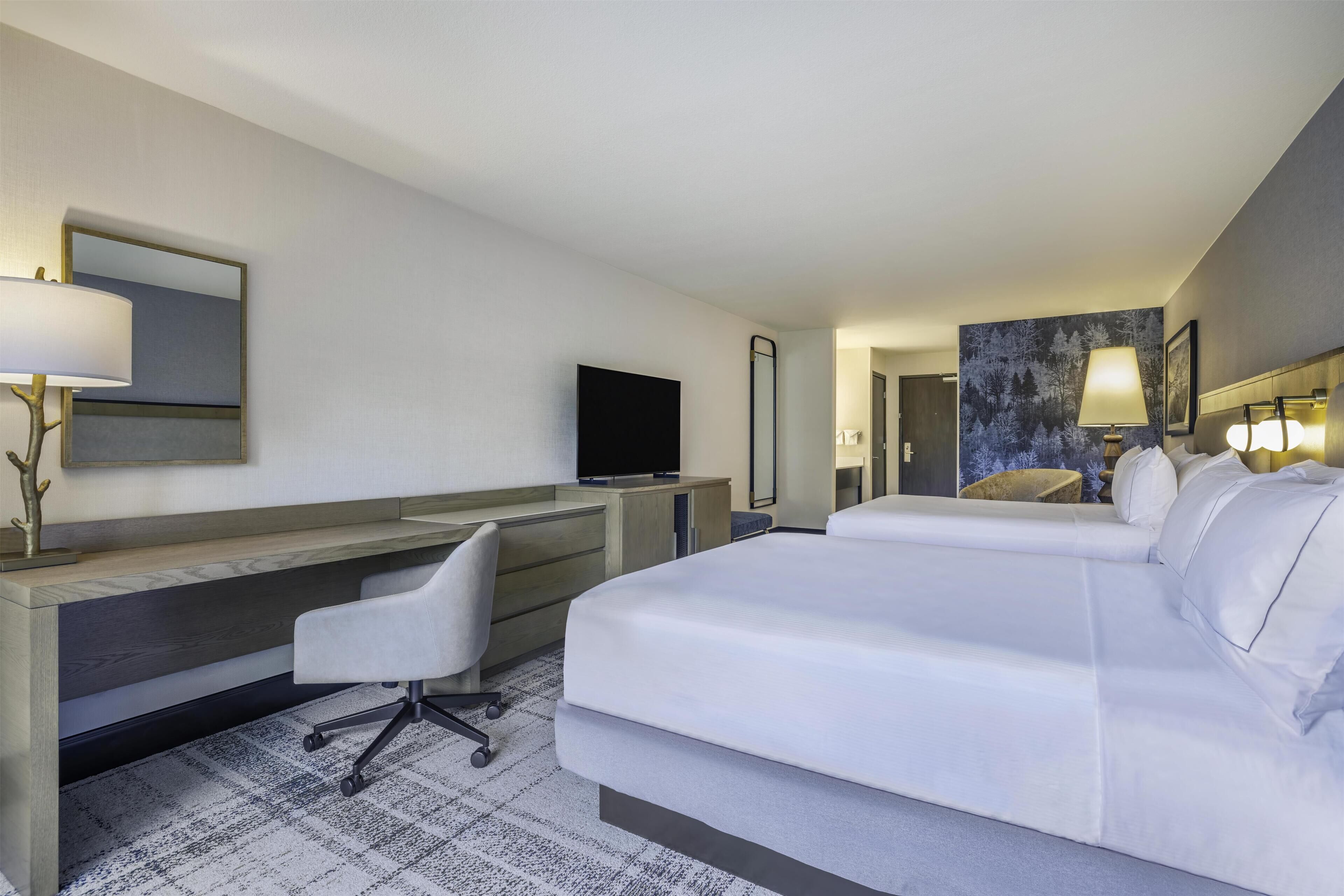 Une chambre d’hôtel équipée d’un lit, d’un bureau, d’une chaise, d’une télévision et d’œuvres d’art accrochées au mur.