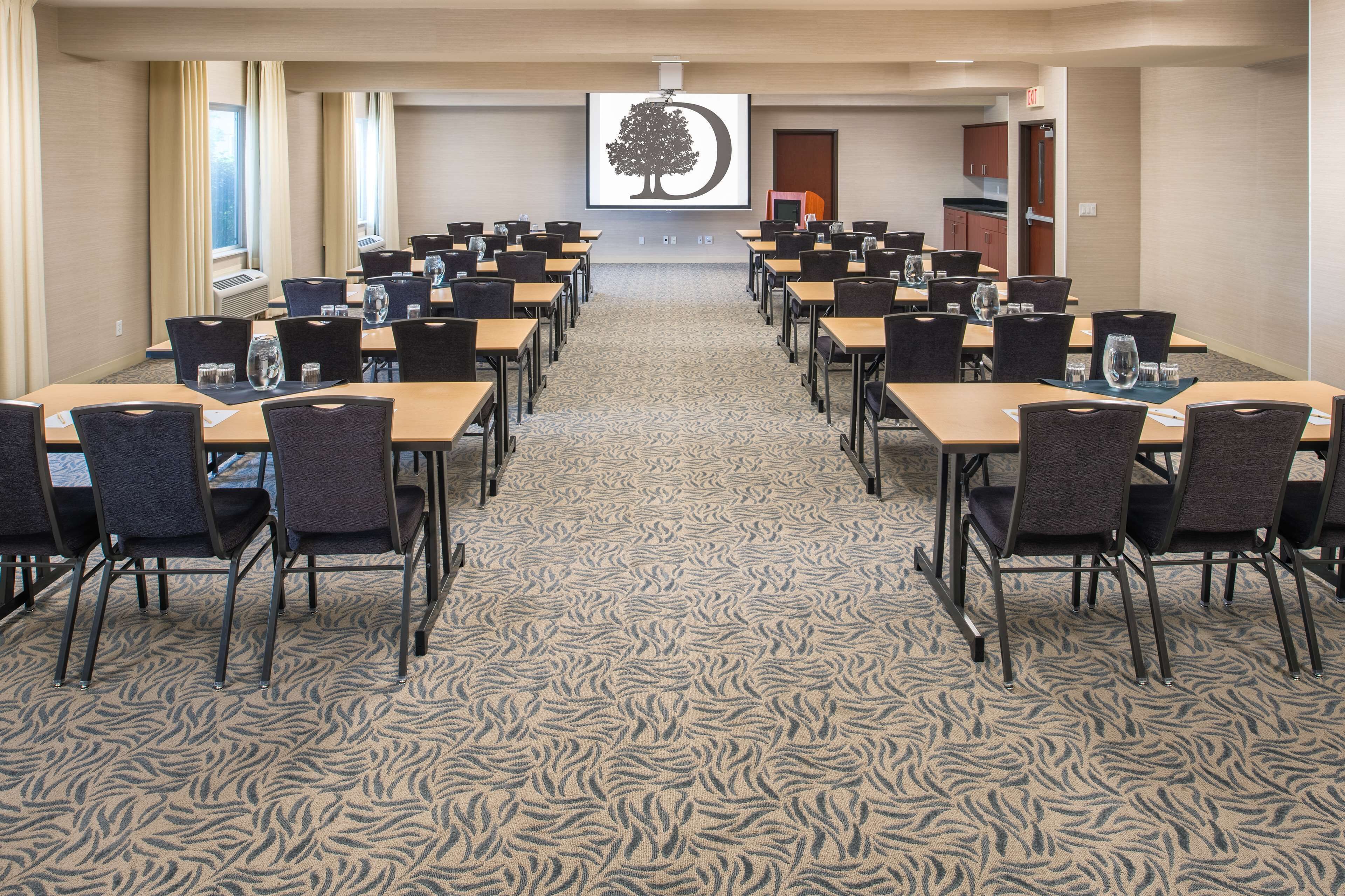 Una sala conferenze con diversi tavoli e sedie, un tappeto decorato e uno schermo di proiezione sullo sfondo.