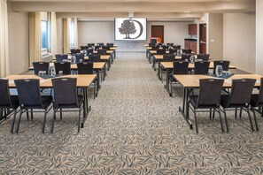 Un salón de conferencias con varias mesas y sillas, un suelo con diseño y una pantalla de proyección al fondo.