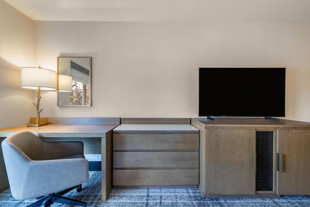 Quarto de hotel moderno com escrivaninha, cadeira, televisão e um espelho grande.