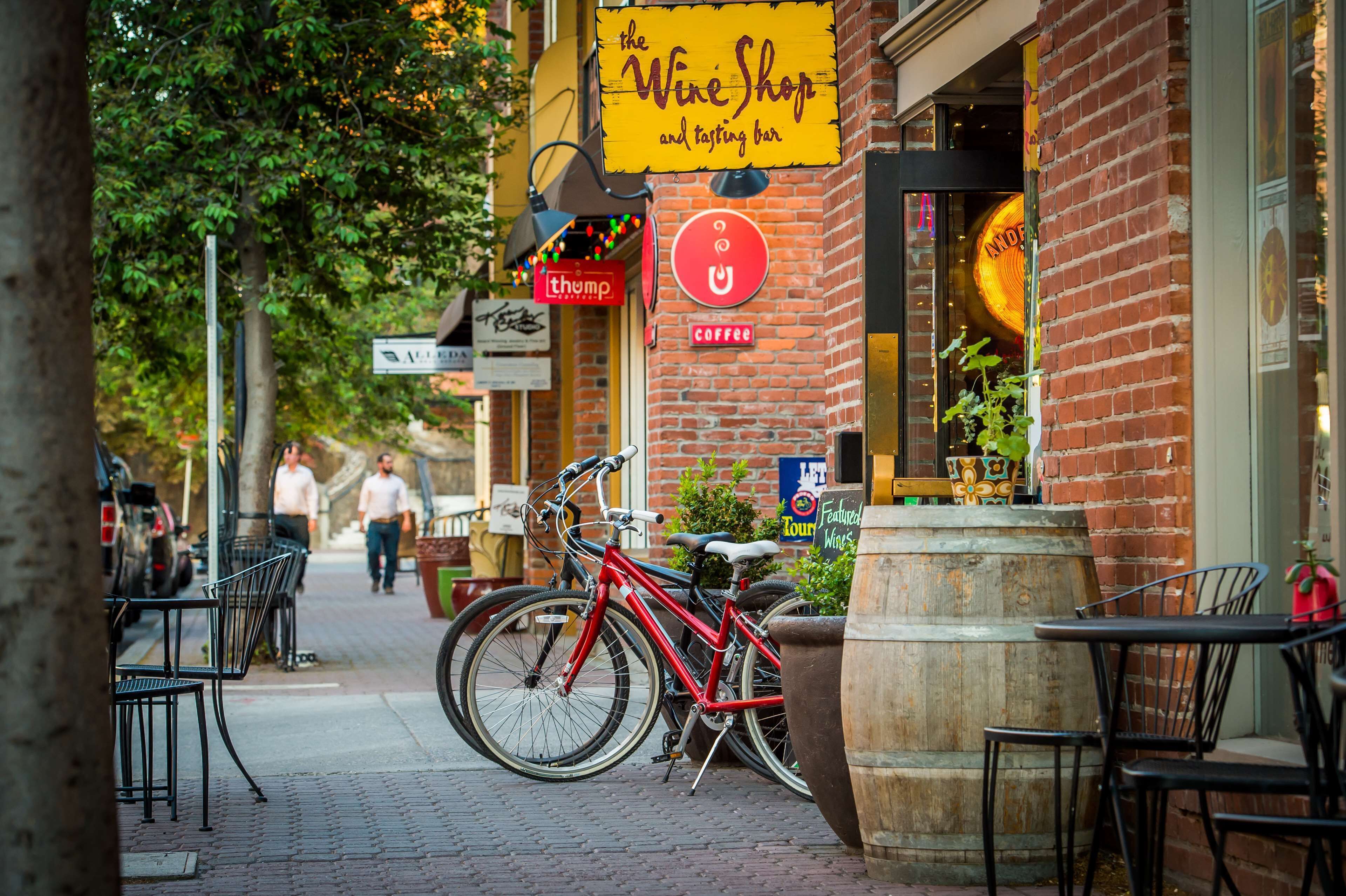 A brick building with a wine shop and tasting bar sign, outdoor seating, and a bicycle parked outside.